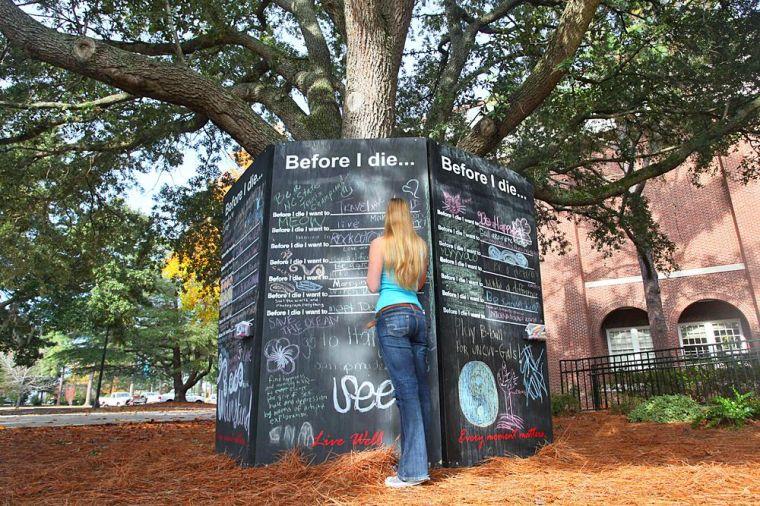 UNCW student Corrine Linder writes on the Before I Die blackboard outside of Trask.