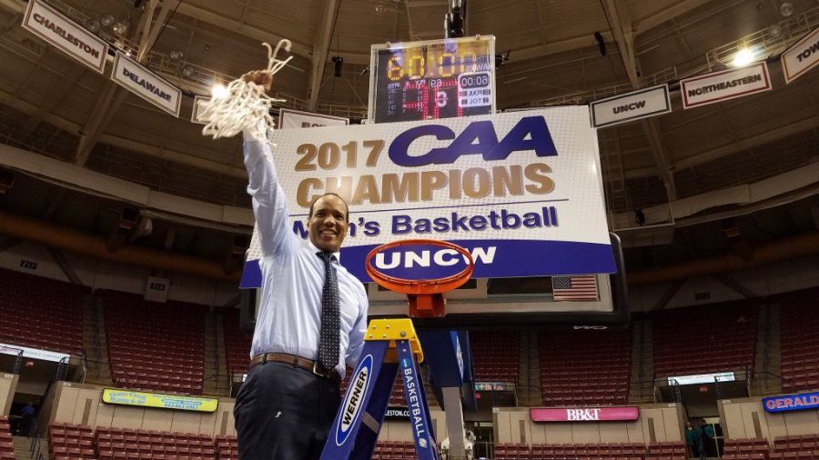 Kevin+Keatts%2C+head+coach+of+the+UNCW+Seahawks%2C+raises+the+game+net+over+his+head+after+winning+a+second+consecutive+CAA+tournament+title.