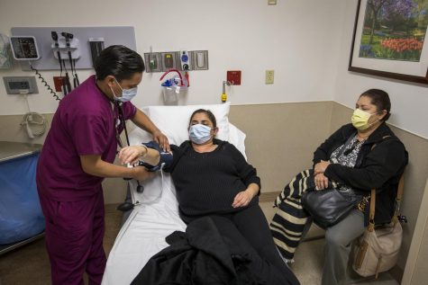 Franz Mirabal, left, patient care technician, takes the blood pressure of Adriana Gudinoperez, a patient with flu symptoms, as Carmen Perez waits with her at right in the emergency room at St. Joseph's Hospital in Orange, Calif., on Friday, Jan. 5, 2018.
