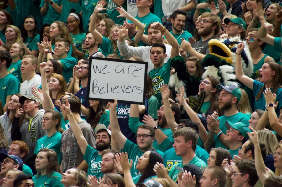 UNC Wilmington students Brent Jansen (low, center-left) and Jacob Denton (low, center-right) hold up their signature whiteboard with the message We are believers in the student section during UNCWs mens basketball game vs. Hofstra on Feb. 10, 2018.