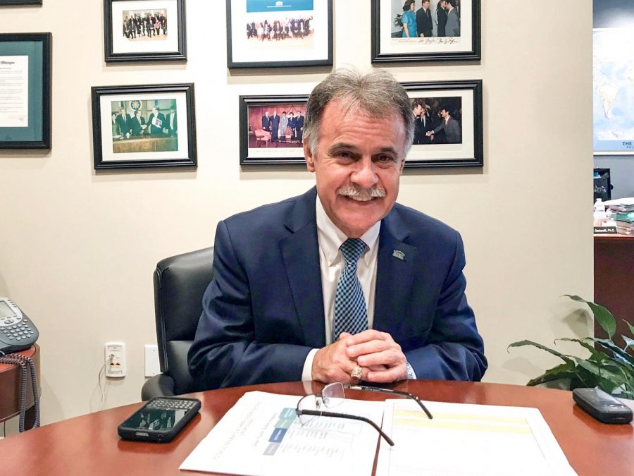 Chancellor Sartarelli at a table in his office, with both of his mobile devices (a Blackberry and a flip phone) as he talks about personal relationships, technology and music.