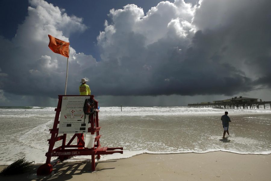 A lifeguard stand on a beach flying the emergency red flag, set against a dark sky in Daytona, FL.