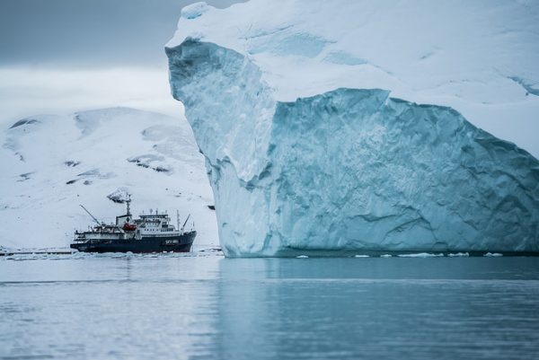 A ship passes by an iceberg off the coast of Greenland. (Hubert Neufeld/Unsplash)