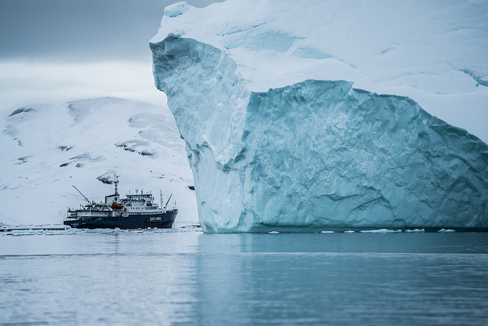 A ship passes by an iceberg off the coast of Greenland. (Hubert Neufeld/Unsplash)