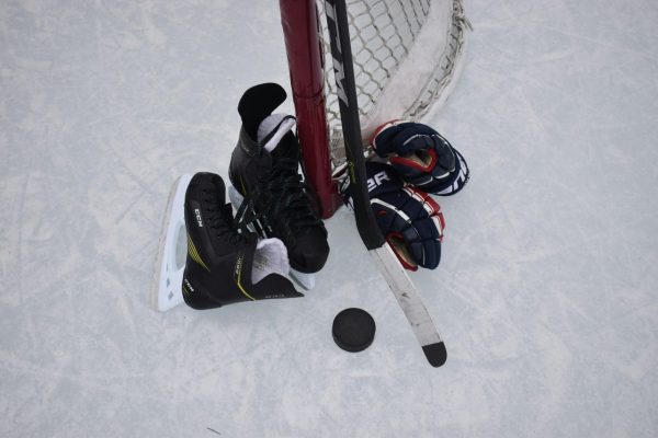 Closeup of a pair of hockey skates, a puck, hockey stick, gloves, and a goal. (Mariah Hewines/Unsplash.com)