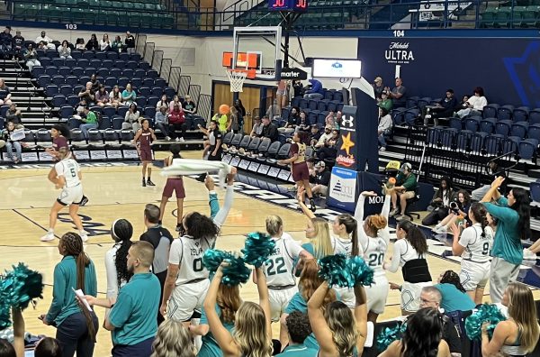 UNCW players cheer on their teammates - UNCW's Alexandra Zelaya waves a towel as she cheers on her teammates from the sidelines. (Addison Lowry/The Seahawk)