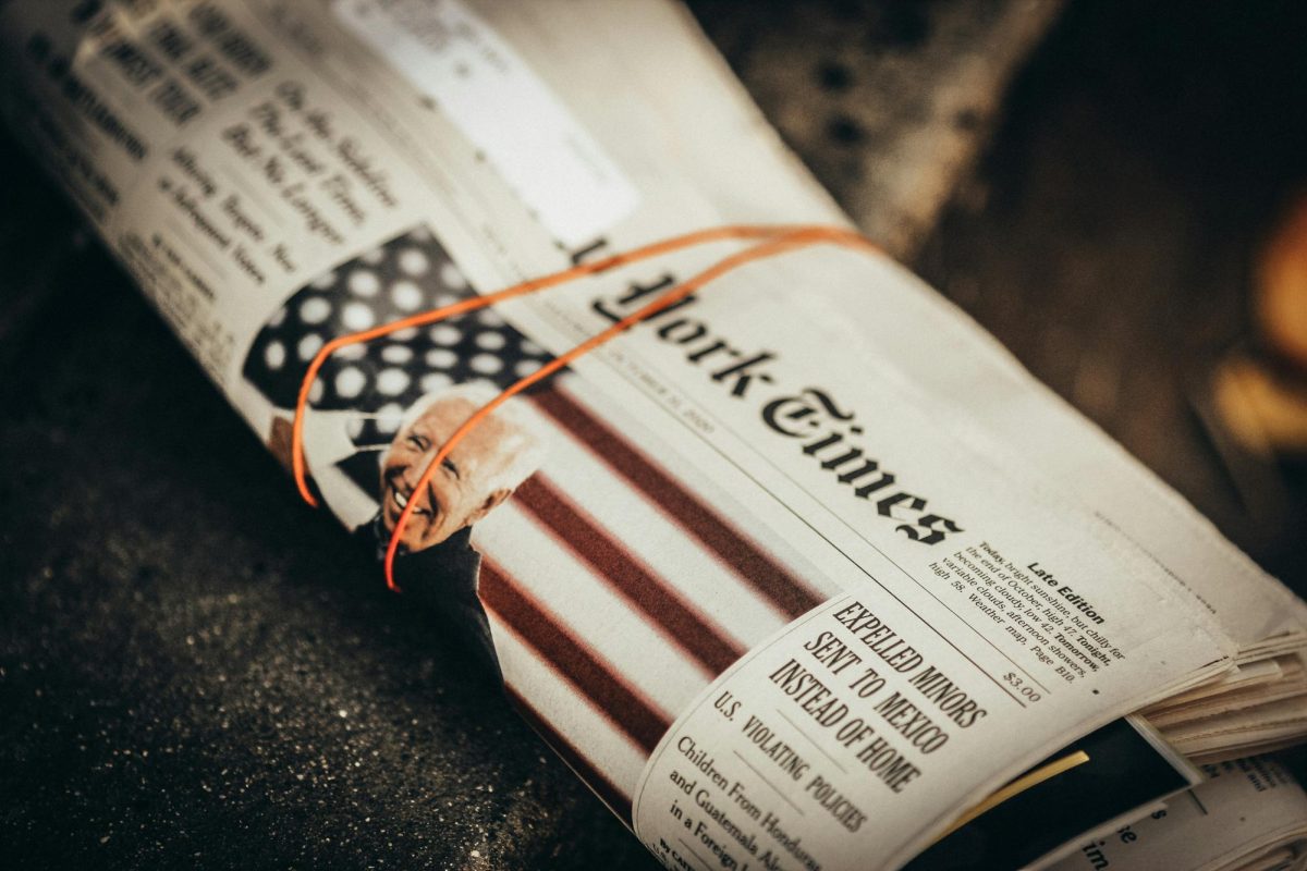 A photo of The New York Times newspaper rolled up on the ground with a featuring photo of former President Joe Biden (Jon Tyson/Unsplash).